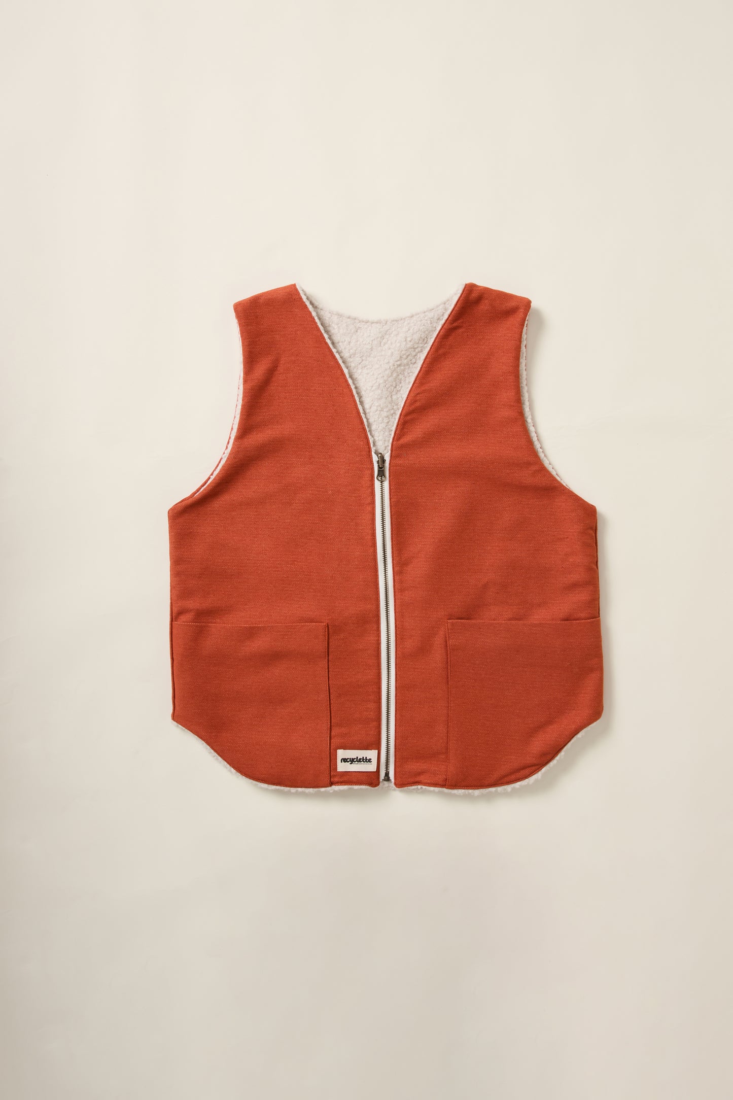 Un gilet réversible rouille d'un coté et crème de l'autre. Denim d'un coté et moumoute de l'autre. Sur un aplat.