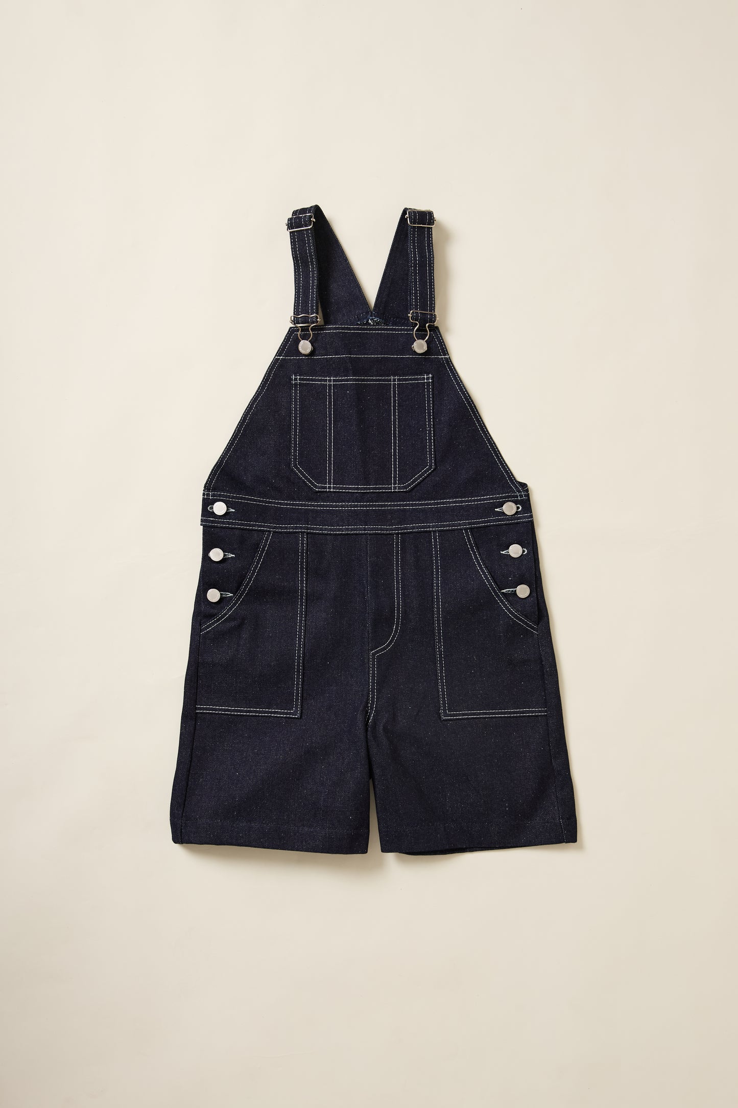 Un aplat de la salopette short denim Recyclette, avec sa grande poche sur le devant et ses deux autres sur le coté et ses bretelles réglabes.