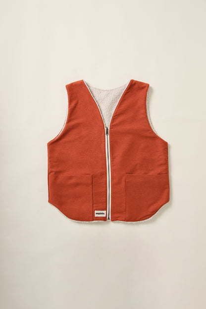 Un gilet réversible rouille d'un coté et crème de l'autre. Denim d'un coté et moumoute de l'autre. Sur un aplat.