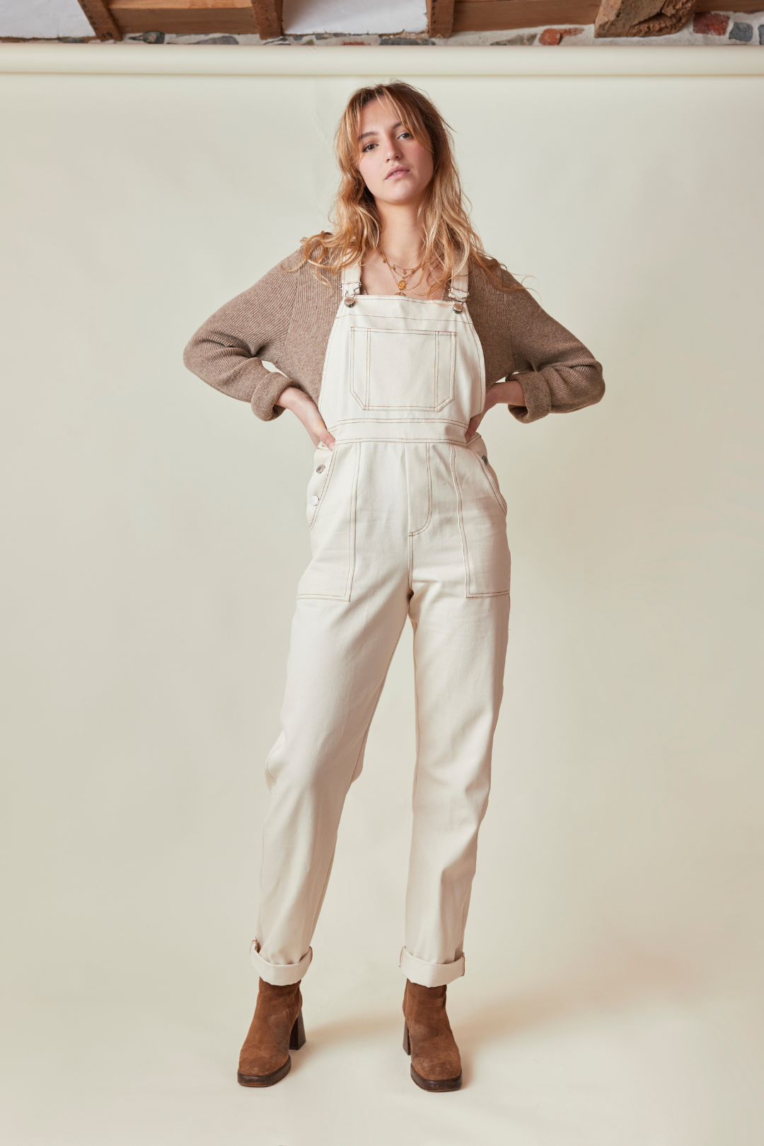 La salopette crème en modèle fernando, avec un pull marron clair et des bottines à talons.