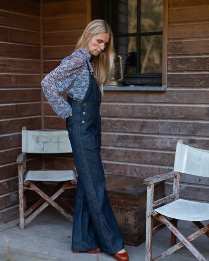 Salopette en denim brut modèle Dancing Queen portée par une mannequin, associée à une blouse fleurie.
