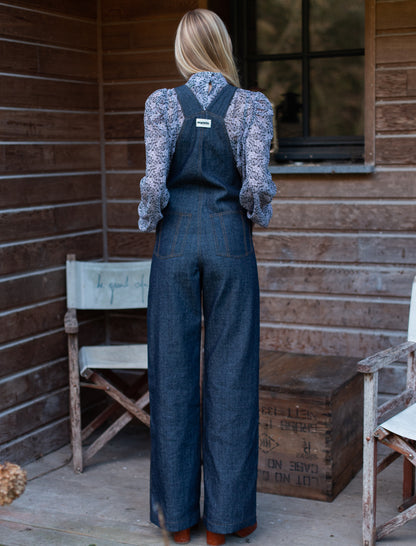 Salopette en denim brut modèle Dancing Queen portée par une mannequin, associée à une blouse fleurie.