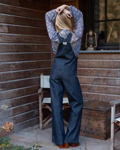 Salopette en denim brut modèle Dancing Queen portée par une mannequin, associée à une blouse fleurie.