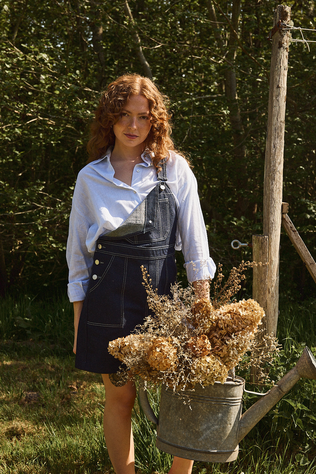 La salopette short denim ouverte, avec une chemise bleue ciel..