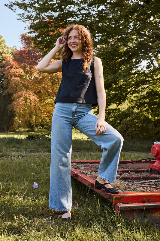 Mannequin portant le top noir avec un jean bleu taille haute et des petites chaussures noires. Look chic Recyclette.