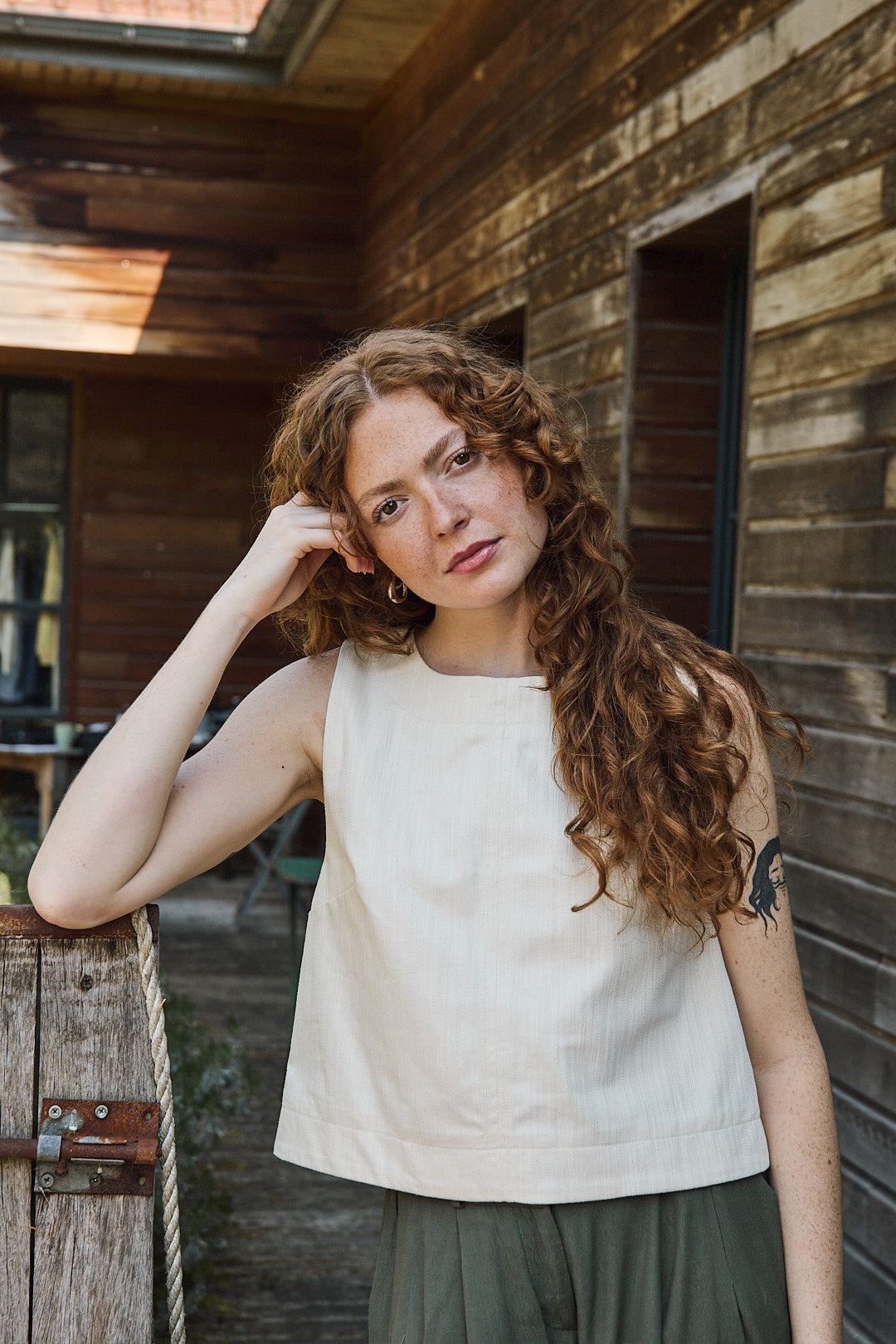 Mannequin portant le top écru avec un pantalon léger ample kaki, pour un look d'été décontracté et élégant.
